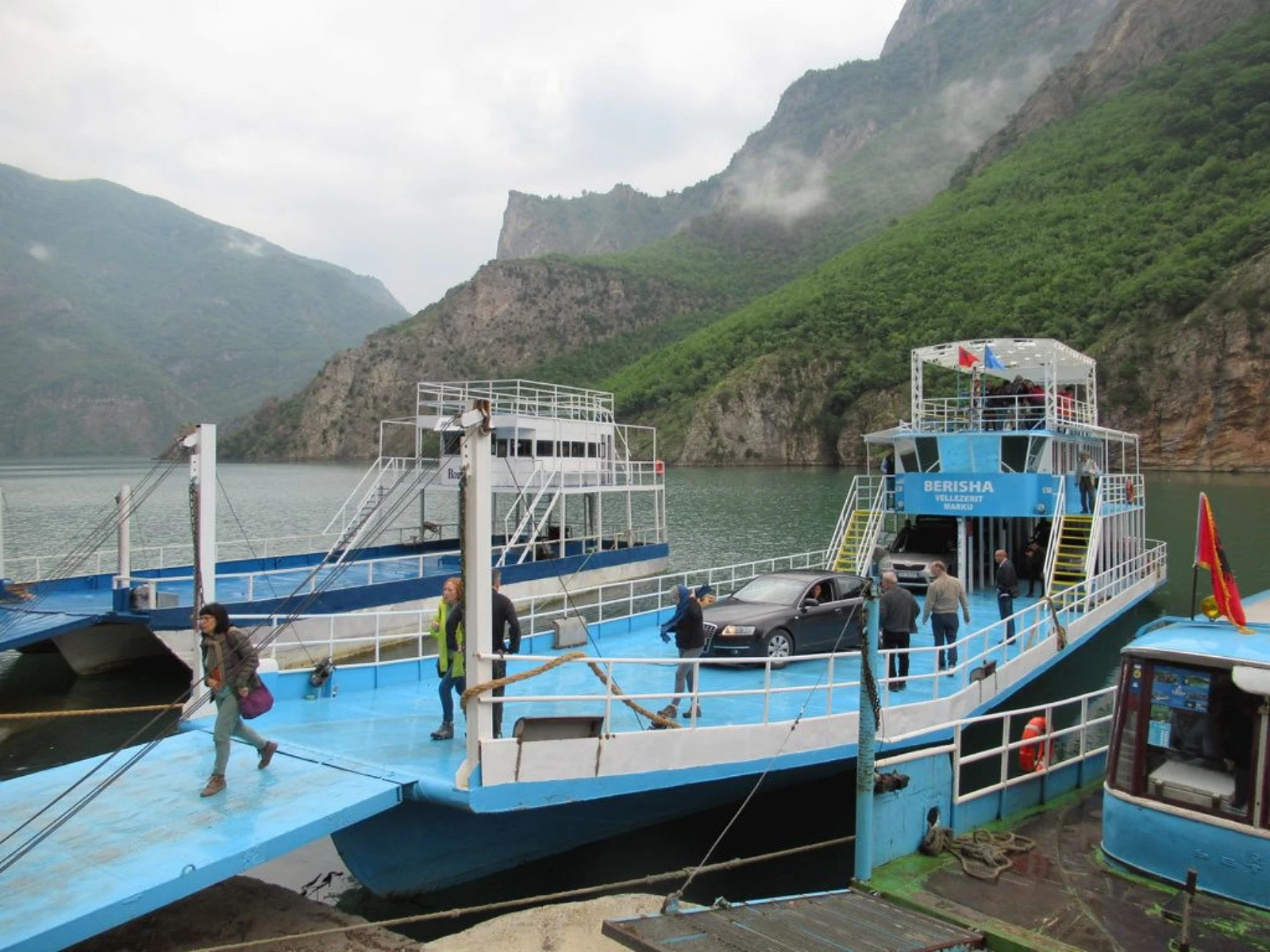 A passenger ferry at Lake Koman, surrounded by steep green Albanian mountains.