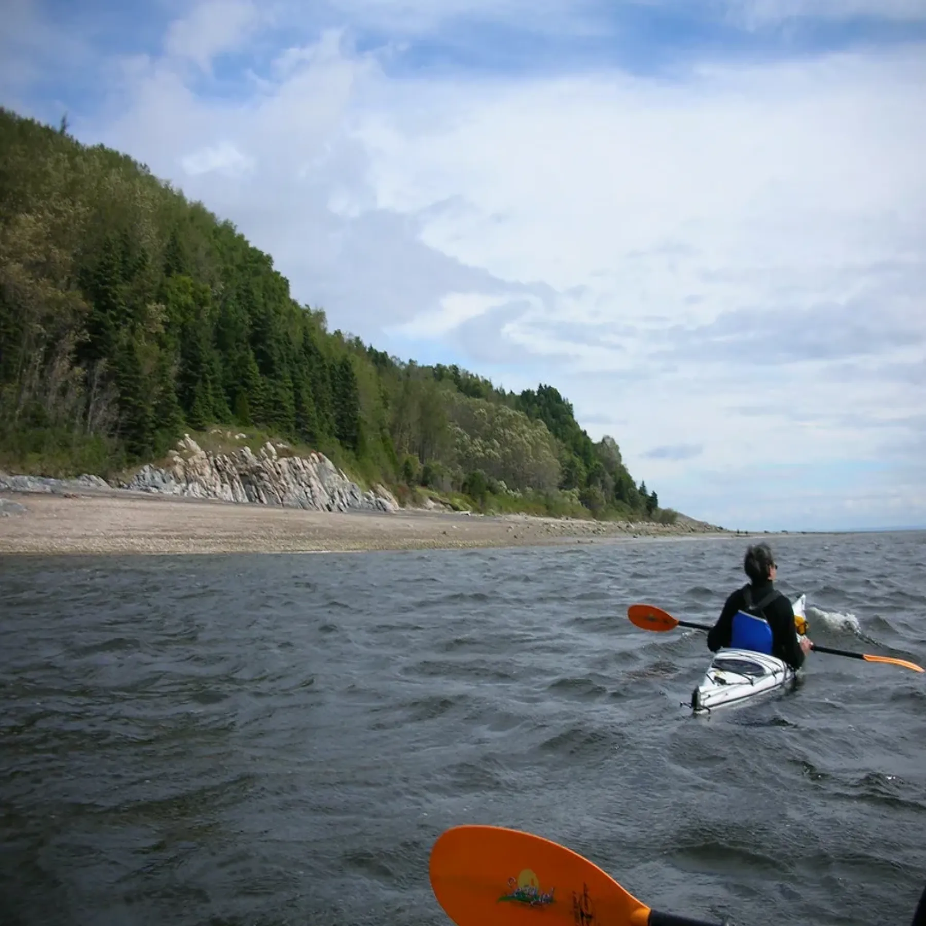 Una persona rema en kayak de mar bajo un cabo boscoso cerca del fiordo de Saguenay.