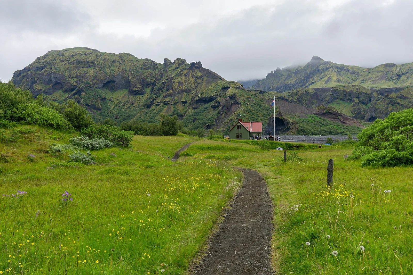 A lone hiker crossing a snowfield beneath dark volcanic hills on Iceland's Laugavegur trail.