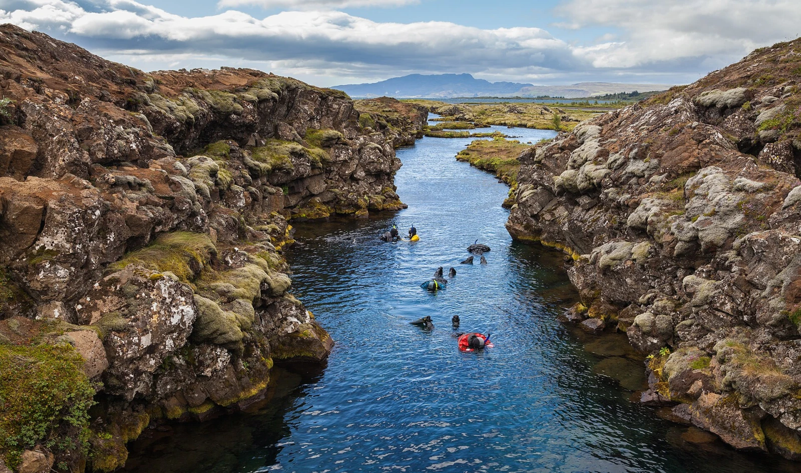 Snorkelers floating in the clear blue water of Silfra's rocky fissure.
