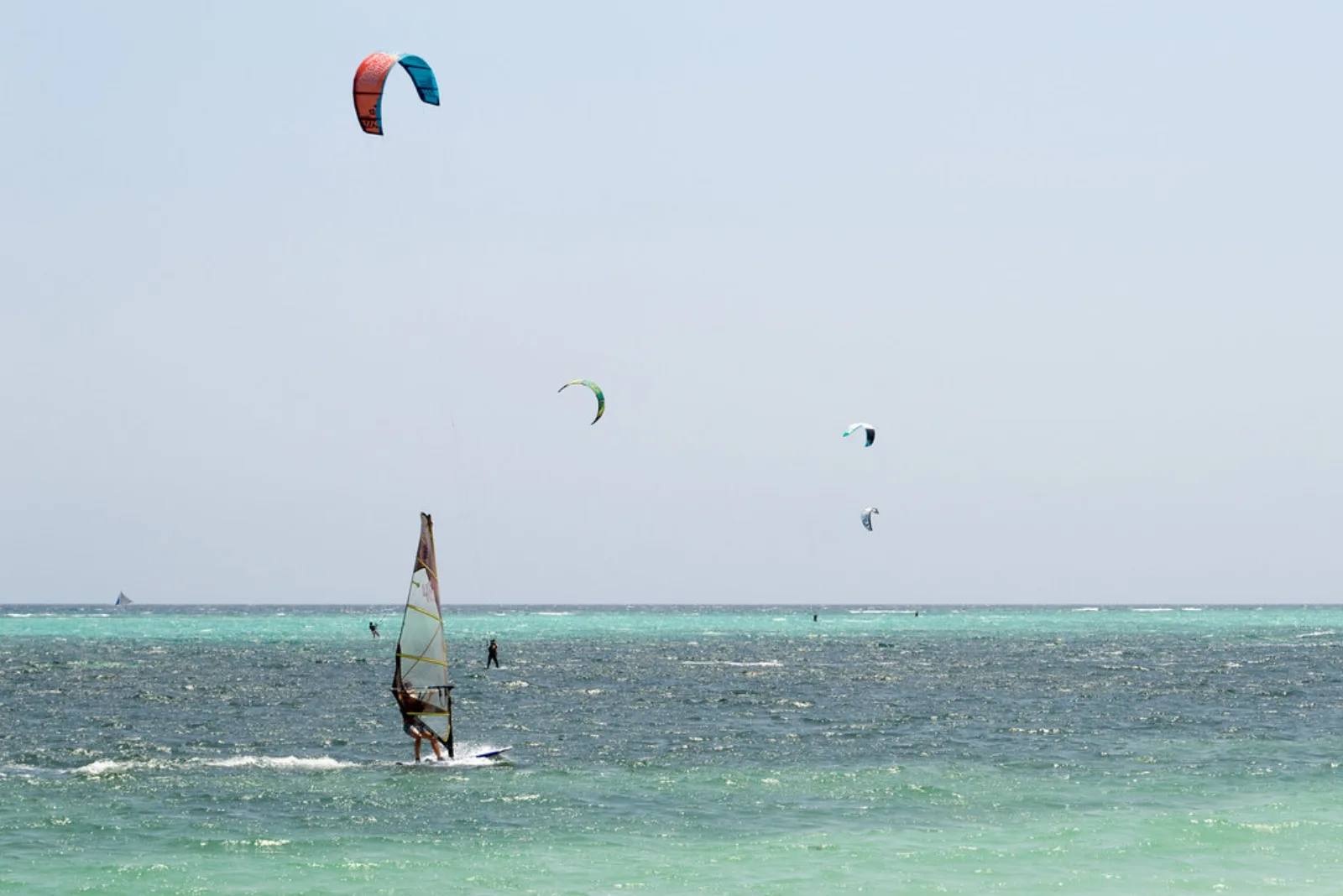 Kitesurfistas y un windsurfista navegan frente a la playa Bulabog.