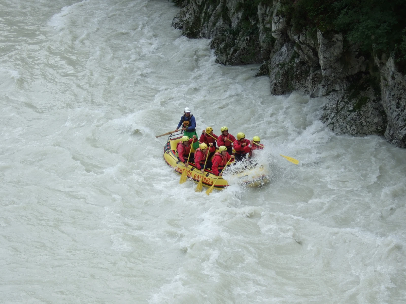 A guided raft carrying paddlers through whitewater on Slovenia's Soča River.