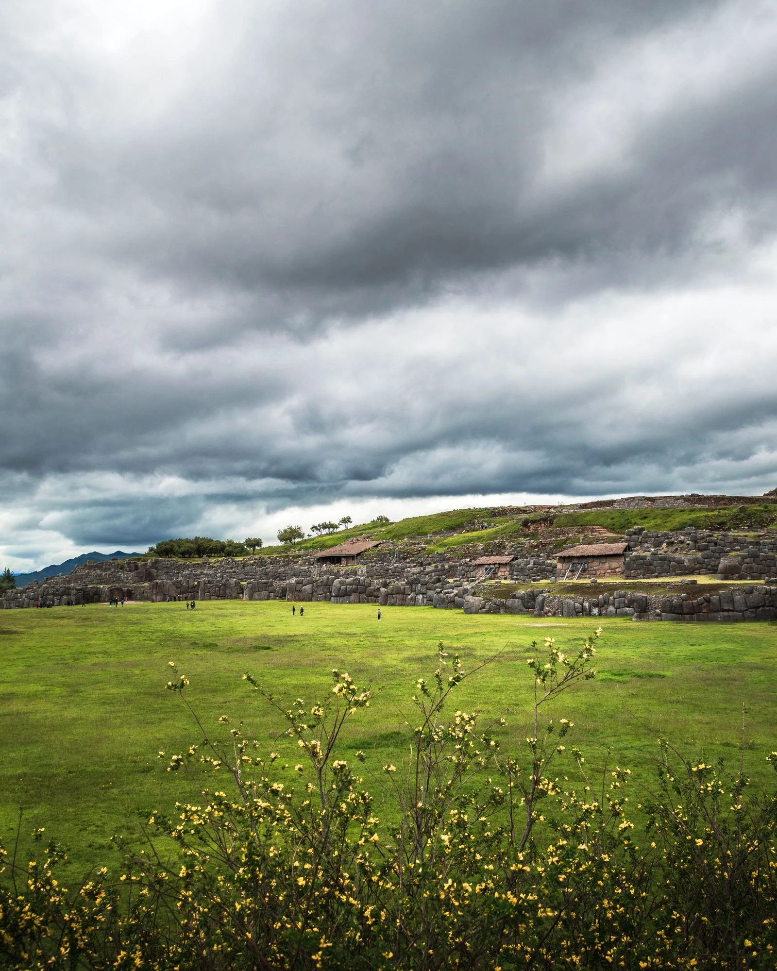 The green ceremonial terraces of Saqsaywaman beneath a stormy Andean sky.