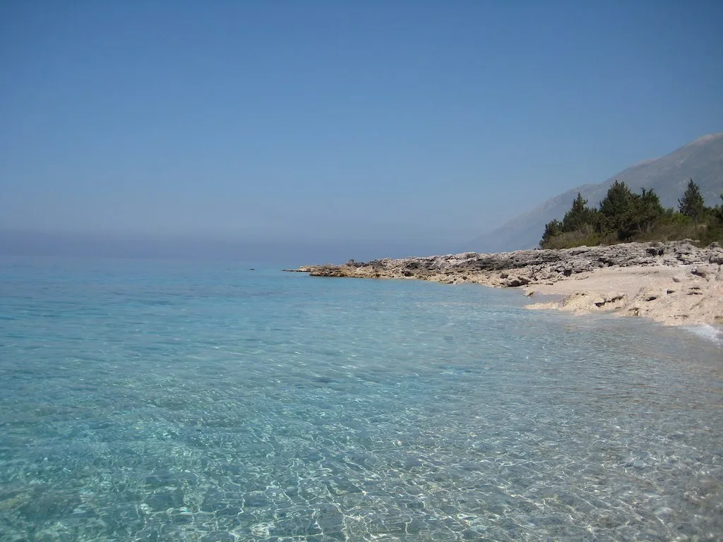 Clear Ionian water beside the pale rocky shore of Dhërmi Beach.