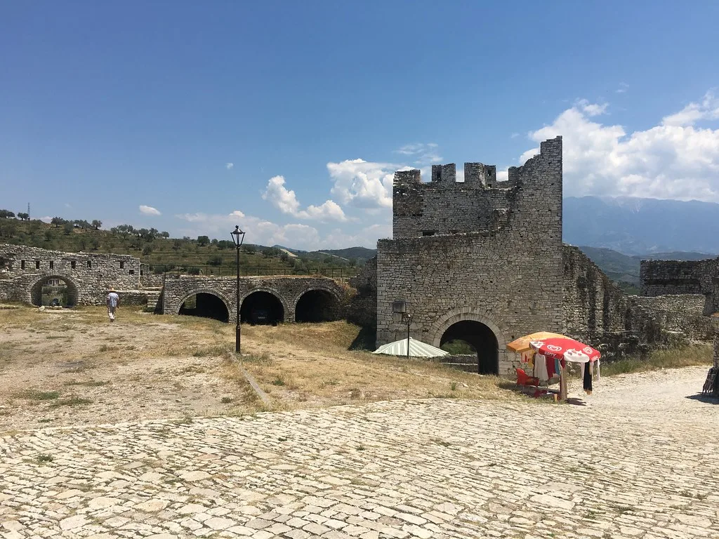 Stone walls and an arched entrance inside Berat Castle under a clear sky.