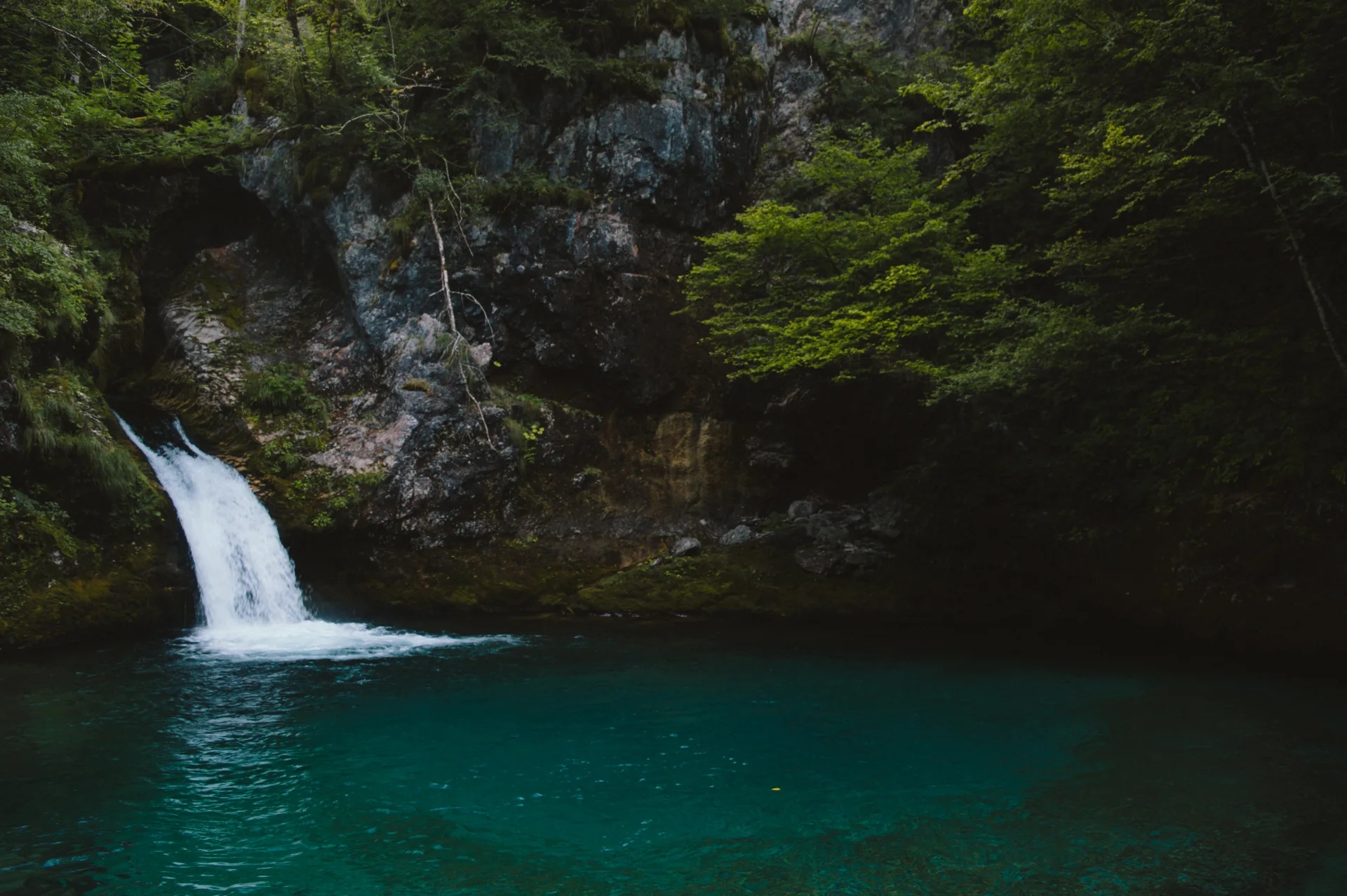 A small waterfall spills into the deep turquoise water of the Blue Eye of Theth.