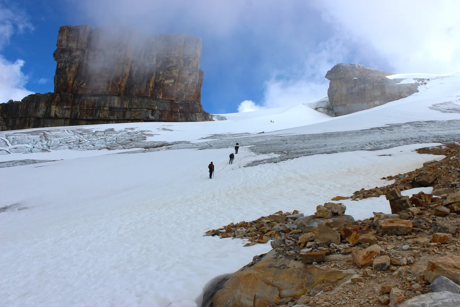 Hikers crossing snow beneath the Púlpito del Diablo rock formations in El Cocuy.