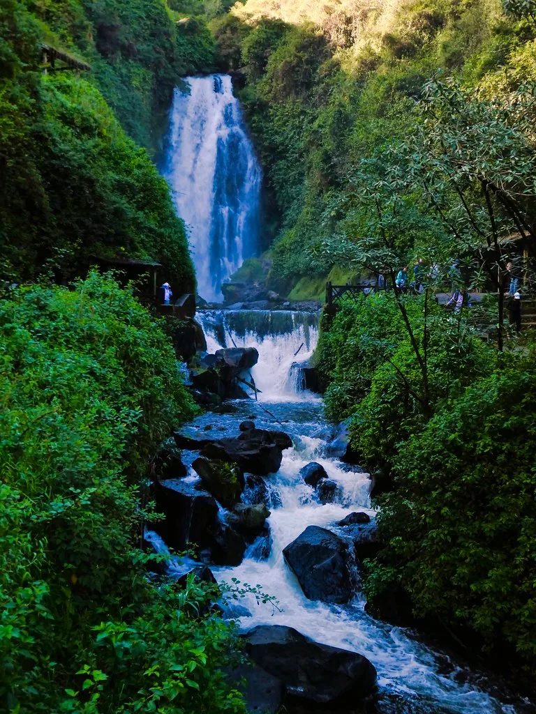 Peguche Waterfall cascading through lush forest beside its visitor path.