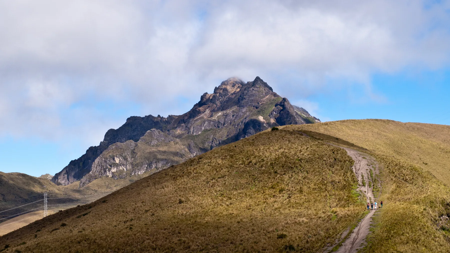 A hiking trail climbing across páramo toward the rocky summit of Rucu Pichincha.