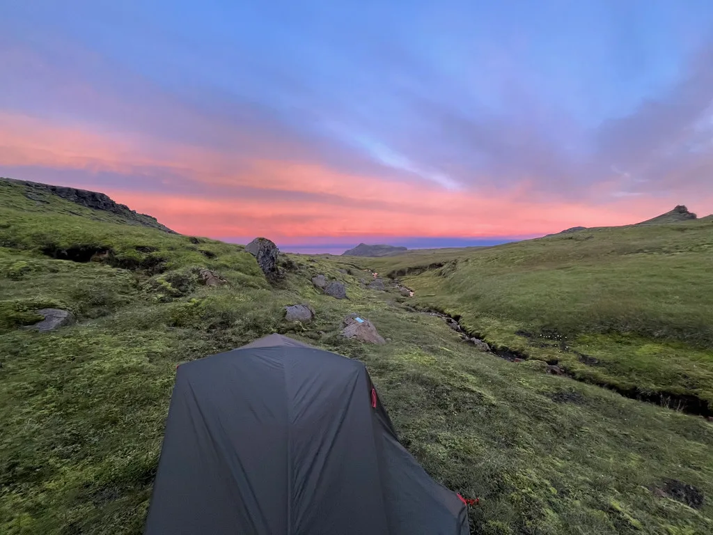 A tent pitched in a green valley along the Fimmvörðuháls route at sunset.