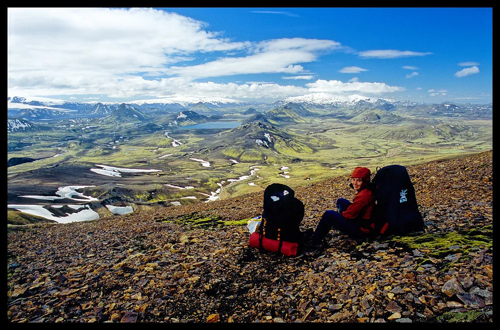 Backpackers resting on a rocky slope above the colorful highlands of the Laugavegur.