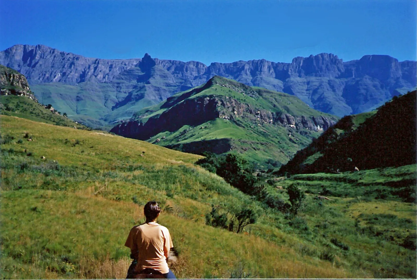A hiker looks toward the peaks and green slopes of the Drakensberg.